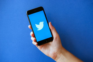 Hand hält Smartphone mit dem Twitter-Logo auf blauem Hintergrund