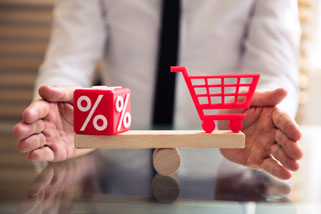 Würfel mit Prozentzeichen und Einkaufswagen im Gleichgewicht auf einer Waage