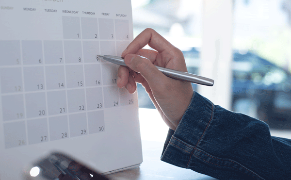 Hand schreibt mit Stift auf Kalender