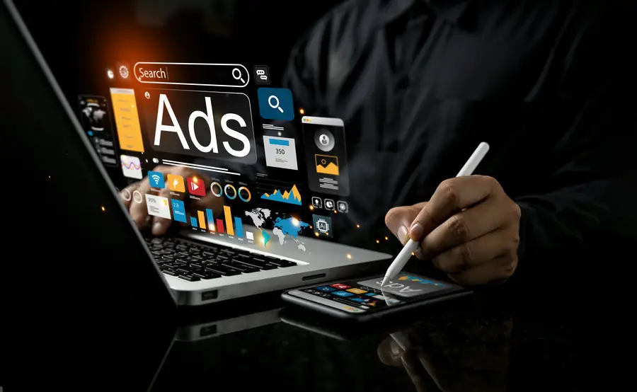 Person arbeitet mit Laptop und Smartphone, digitale Anzeigen- und Marketing-Symbole schweben über den Geräte